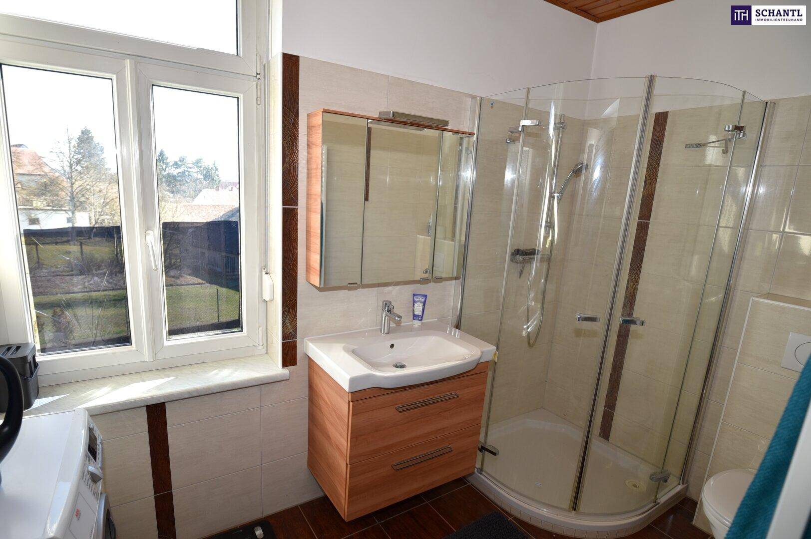 Helles Badezimmer mit Dusche, Fenster und Holzwaschtischunterschrank.