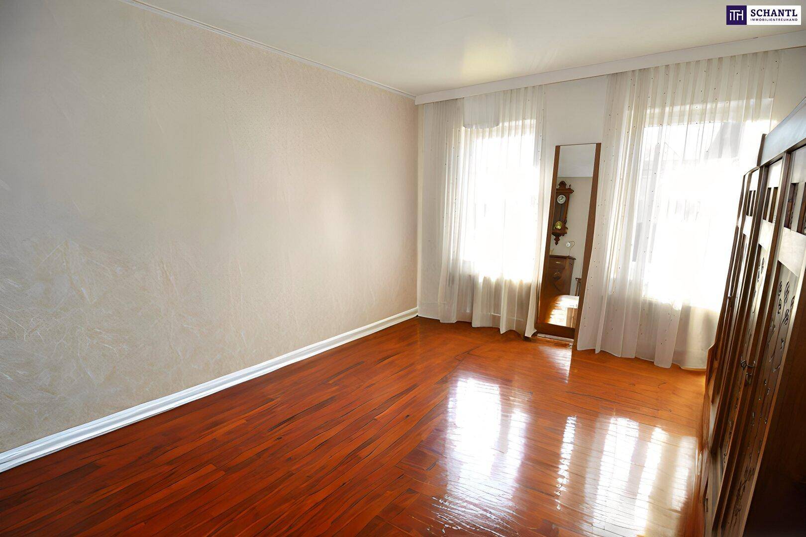 Helles Schlafzimmer mit glänzendem Holzboden und großen Fenstern mit Vorhängen.