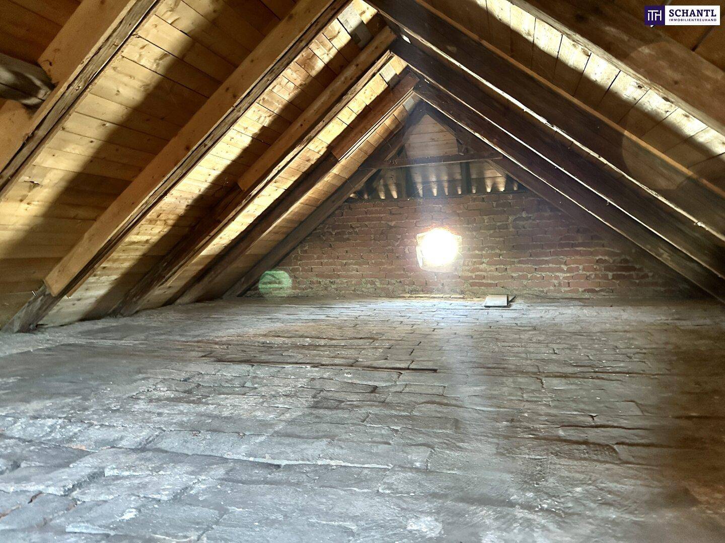Unausgebauter Dachboden mit sichtbaren Holzbalken und Ziegelboden.