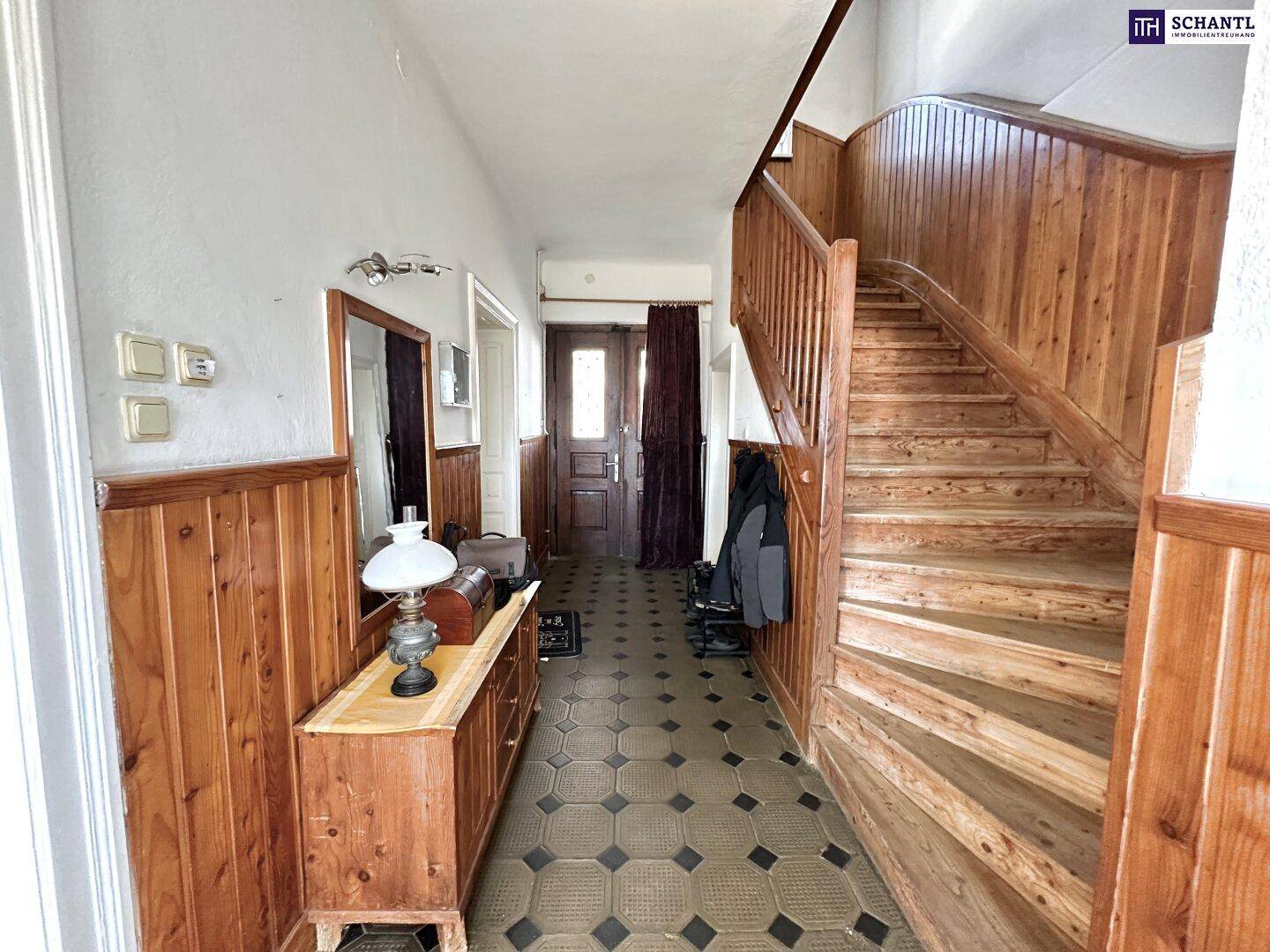 Geräumiger Eingangsbereich mit Holztreppe, Holzvertäfelung und gemustertem Fliesenboden.