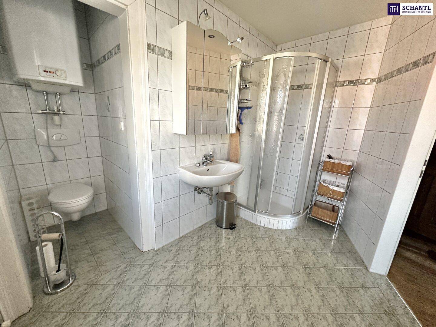 Badezimmer mit Dusche, WC und hellen Fliesen an Wänden und Boden.