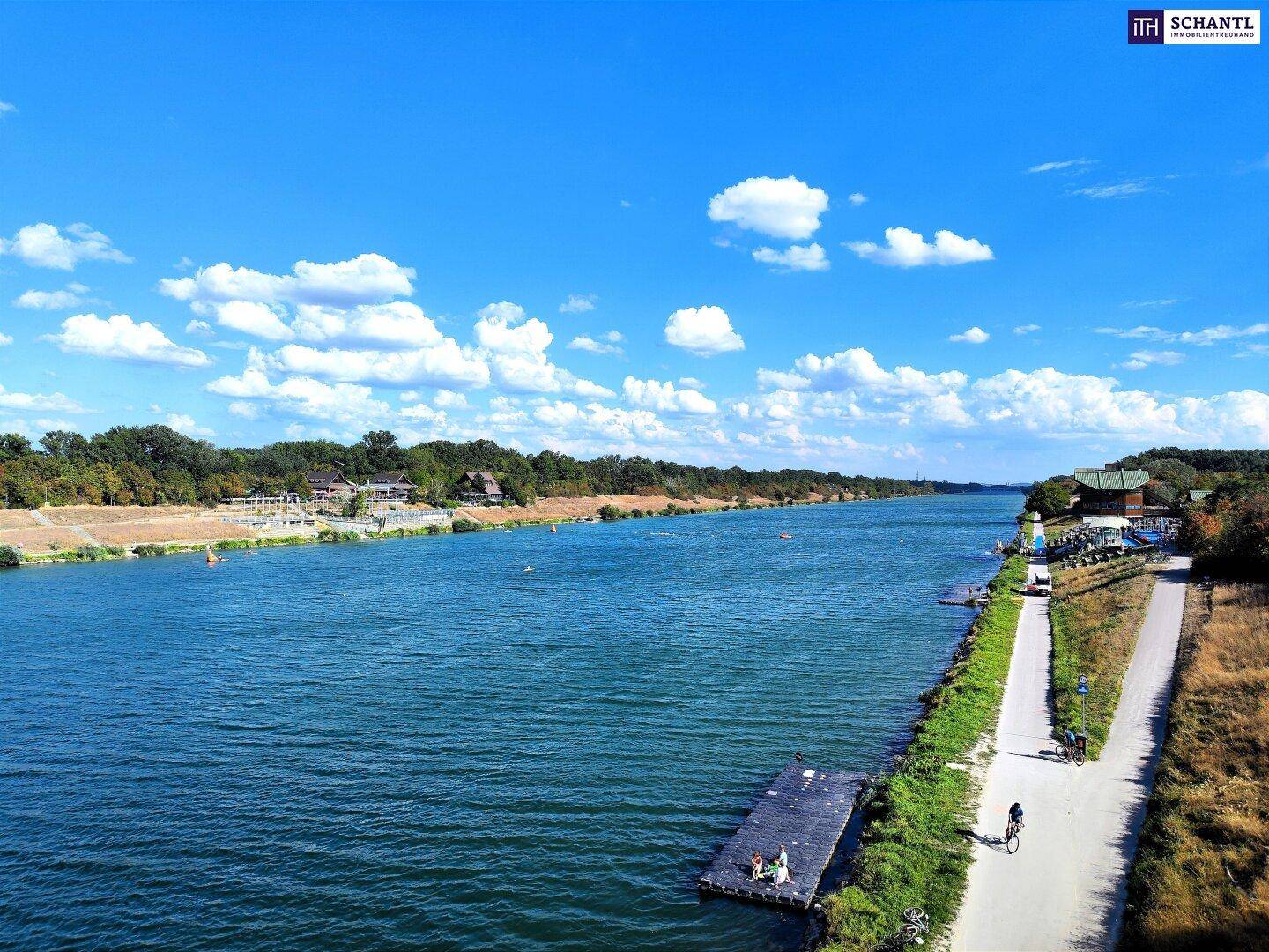 Breiter Fluss oder Kanal mit Uferweg, umgeben von Grünflächen und Freizeitmöglichkeiten am Wasser.
