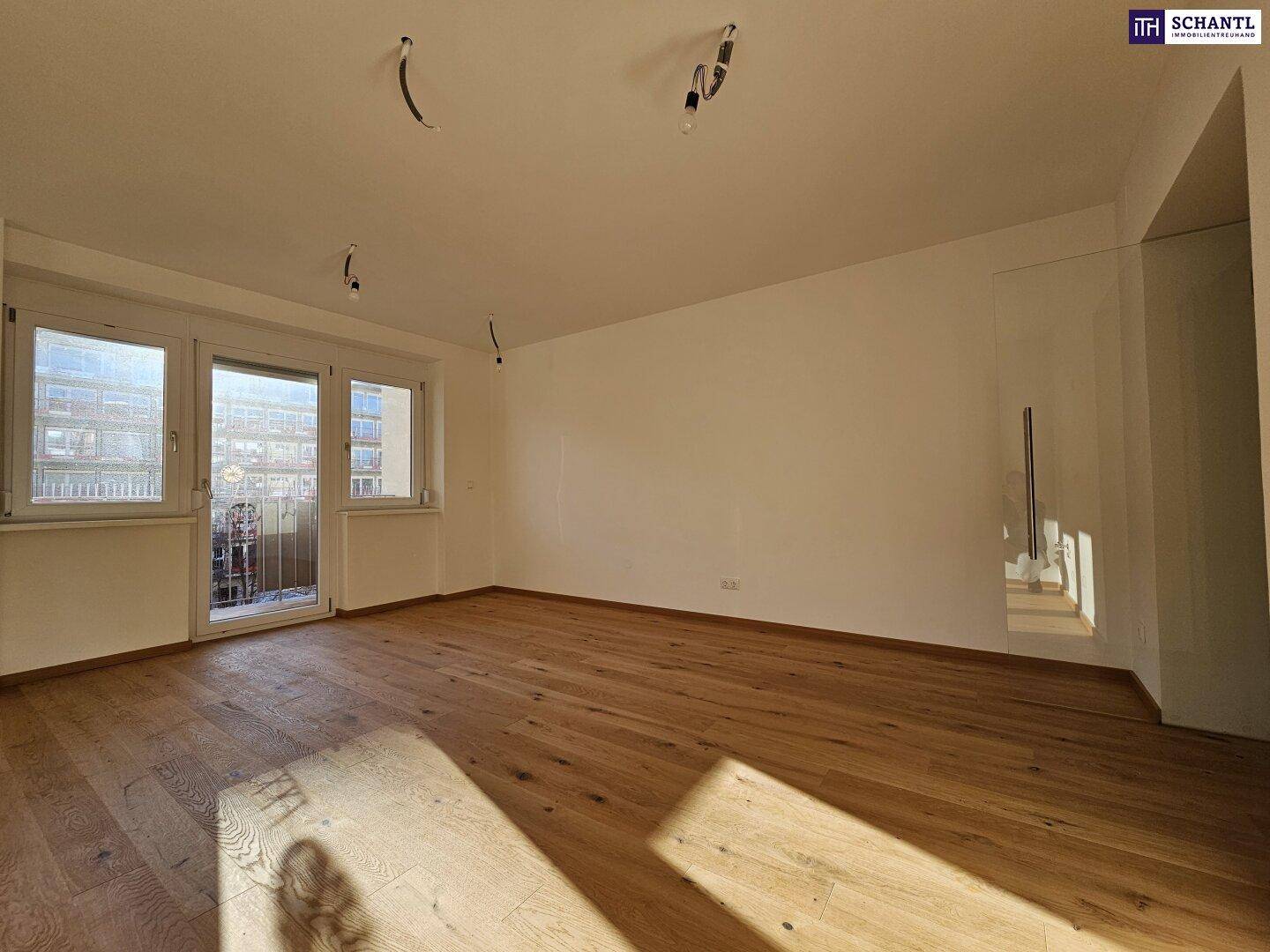 Geräumiges Wohnzimmer mit Holzboden und großen Fenstern, die viel Tageslicht hereinlassen.