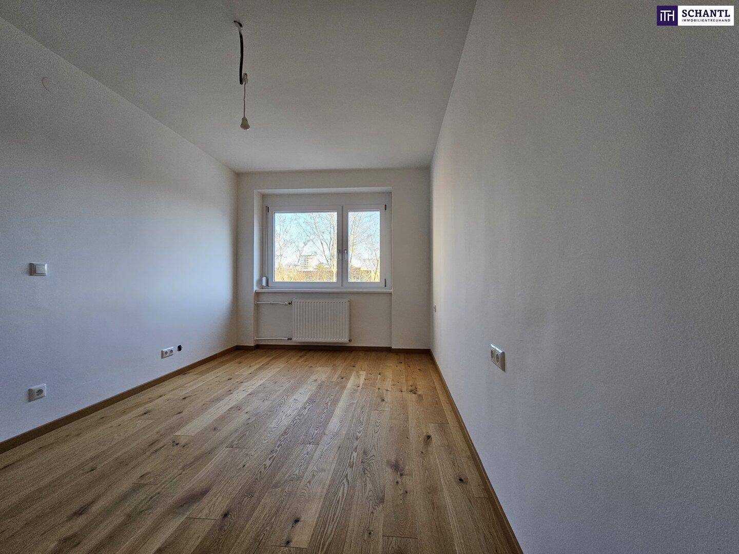 Helles Zimmer mit Parkettboden und Fenster, das viel Tageslicht hereinlässt.
