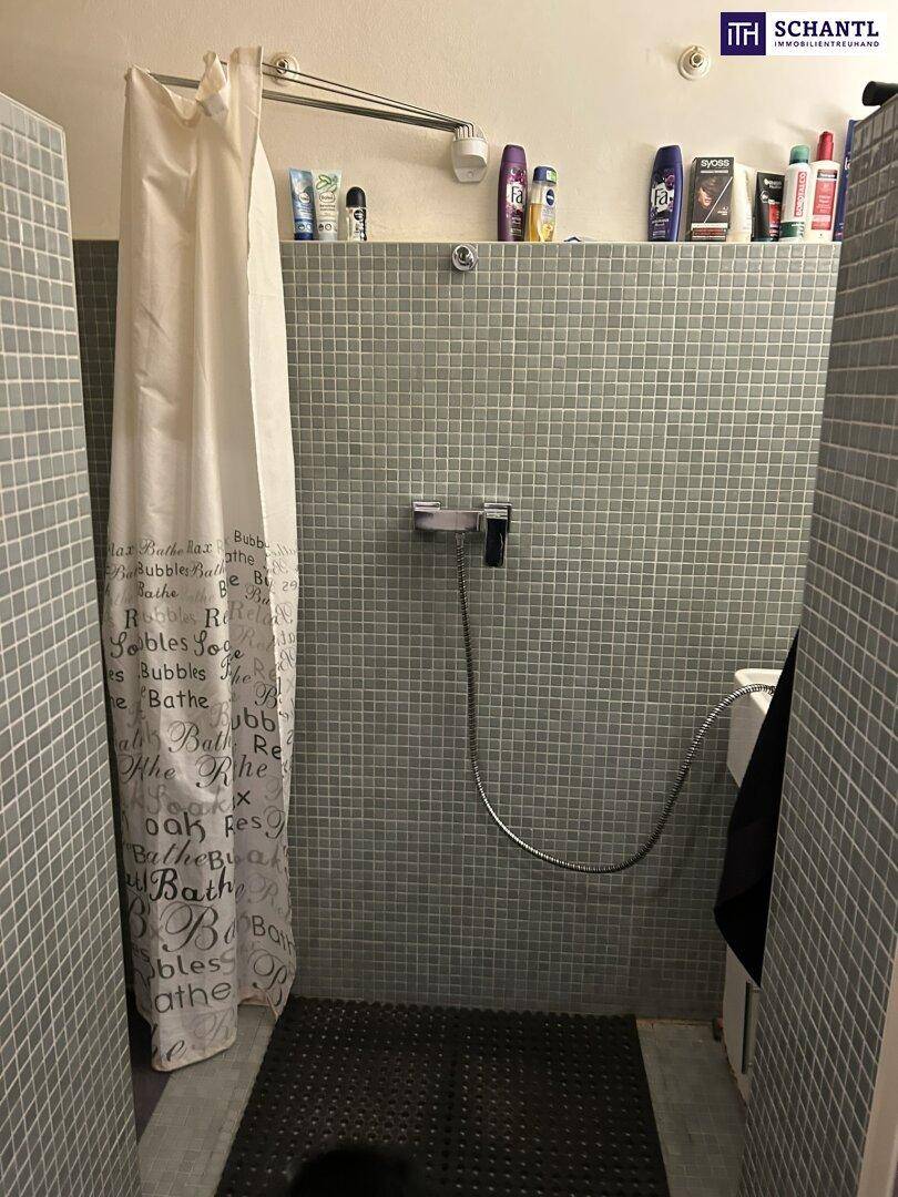 Badezimmer mit Duschbereich, grauen Fliesen und Duschvorhang.