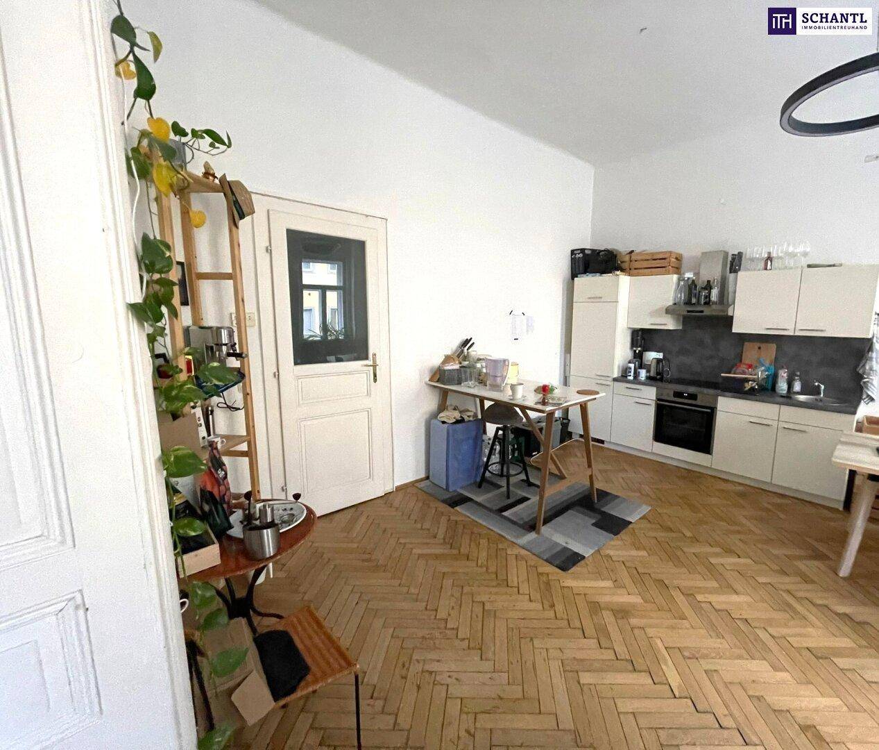 Geräumiger Wohnbereich mit kleiner Küchenzeile, Holzboden und viel Tageslicht.