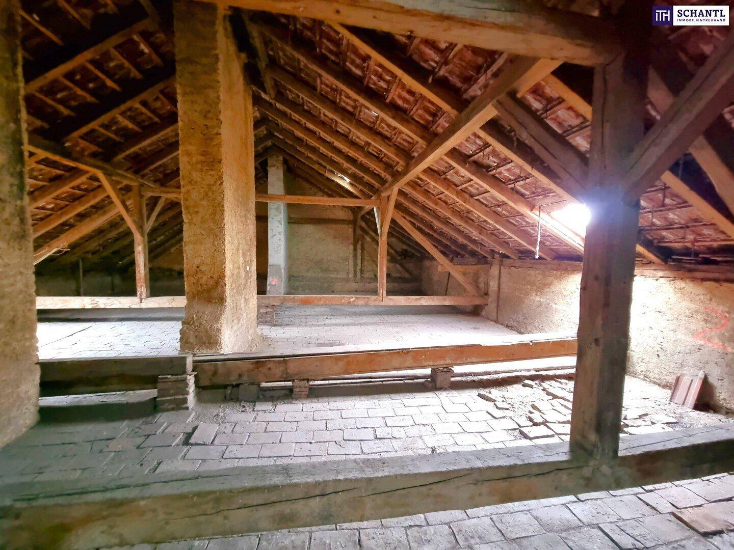 Geräumiger Dachboden mit sichtbaren Holzbalken und Ziegeln, bereit für den Ausbau.