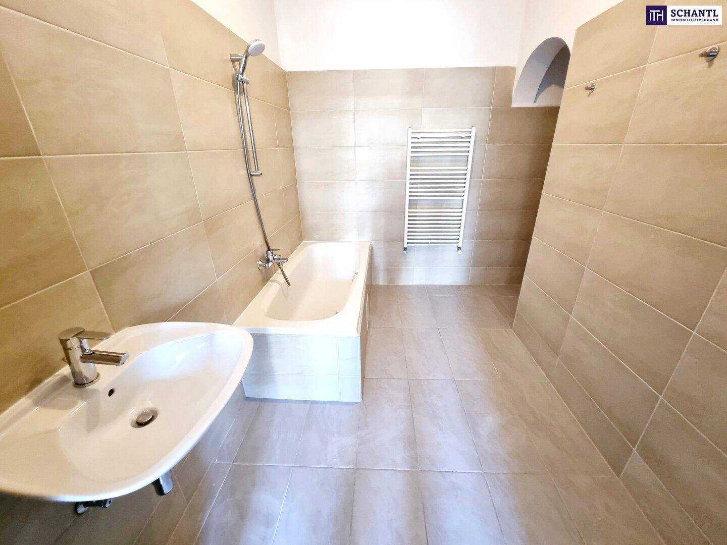 Modern gefliestes Badezimmer mit Badewanne, Waschbecken und beheiztem Handtuchhalter.