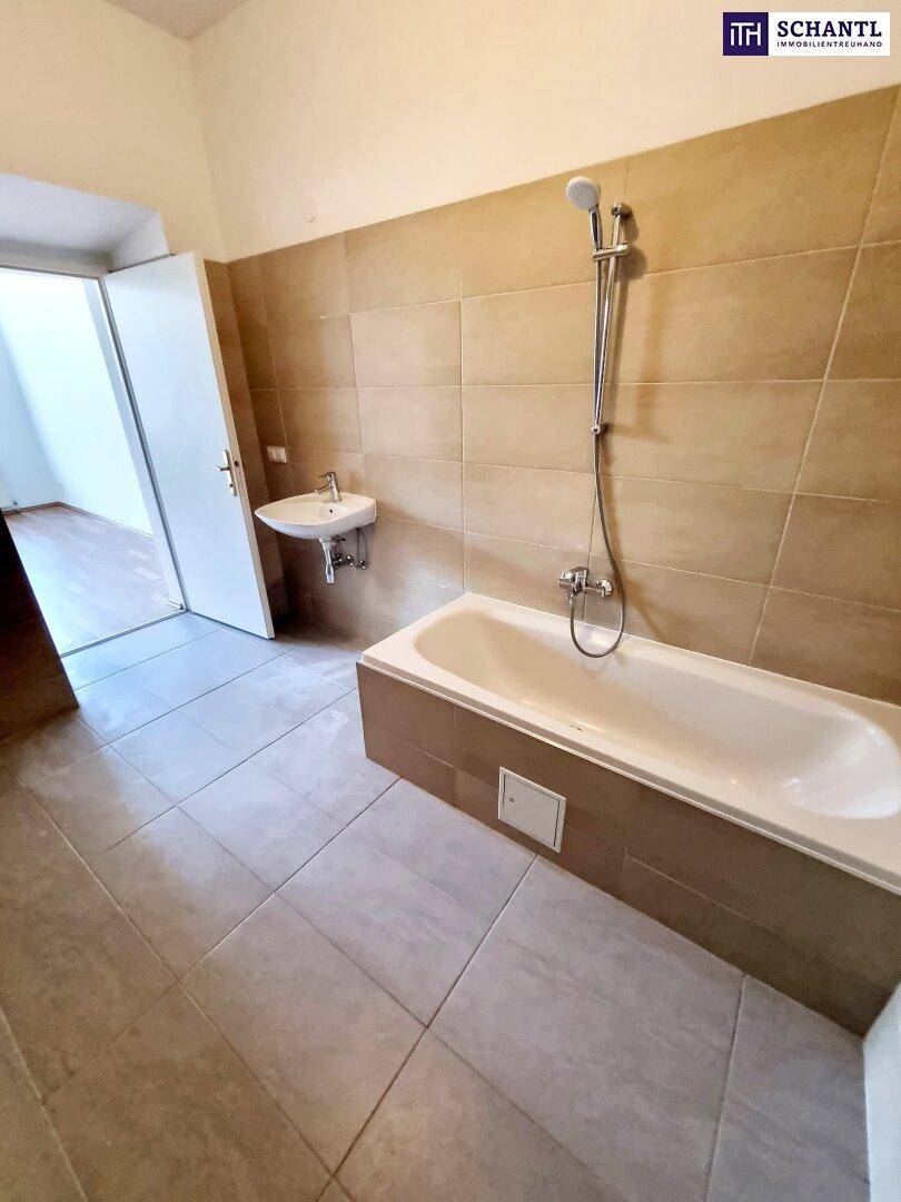 Helles Badezimmer mit beigefarbenen Fliesen, Badewanne und Waschbecken.