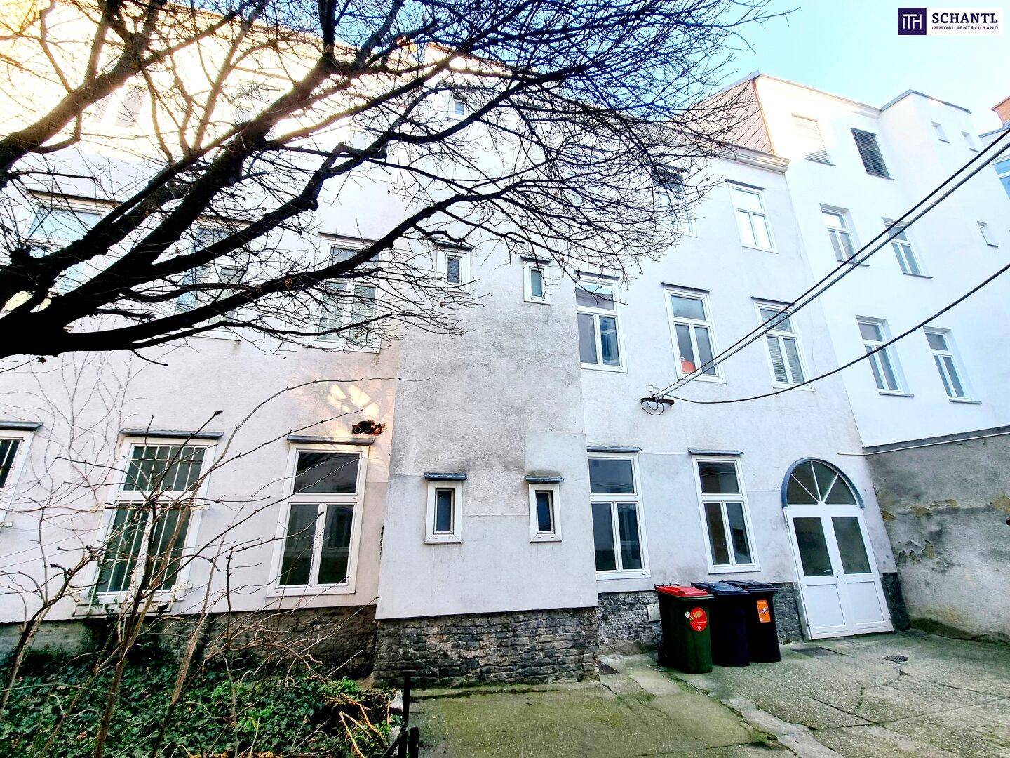 Rückseite eines Gebäudes mit verschiedenen Fenstern und einem kleinen Hofbereich.
