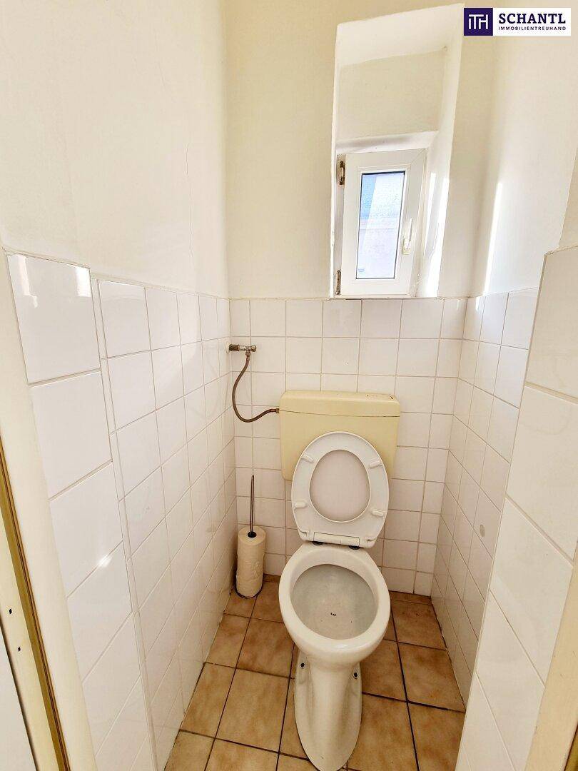 Separate Toilette mit Fenster, weißen Fliesen und einem älteren Spülkasten.
