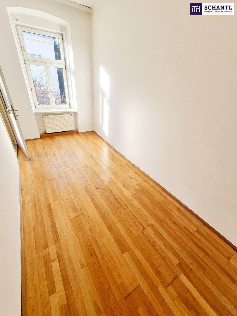 Heller Raum mit Holzboden und weißen Wänden, durch ein Fenster fällt viel natürliches Licht.