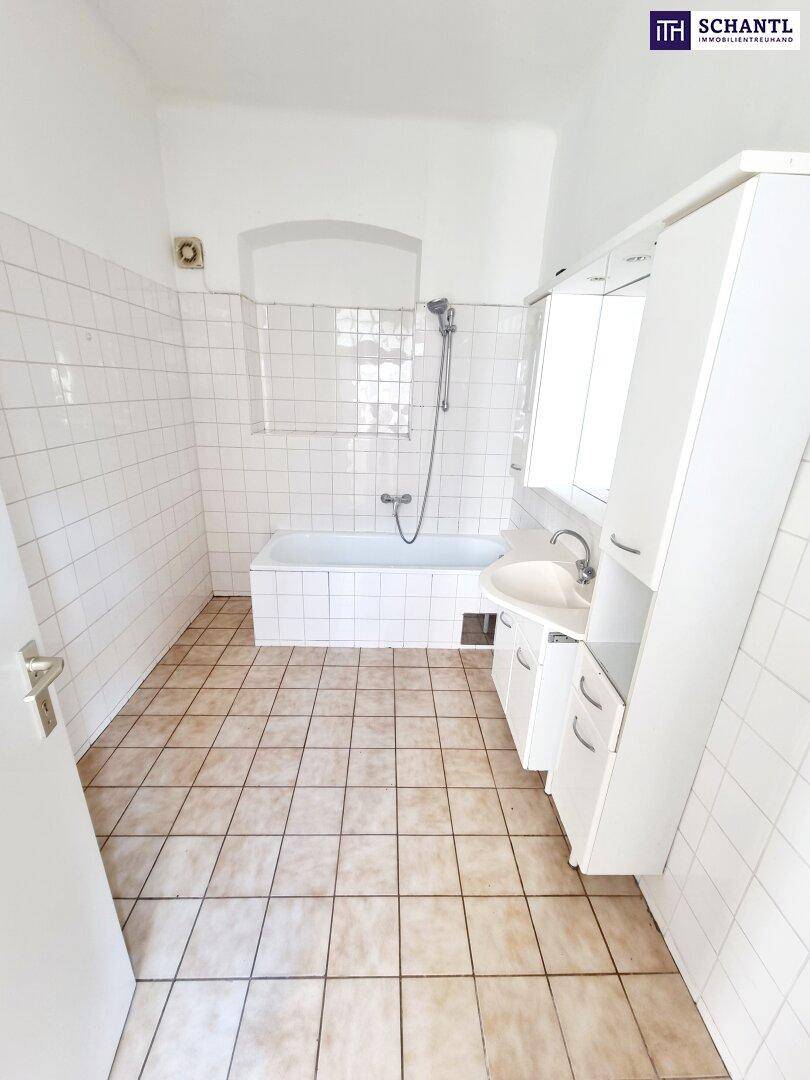 Badezimmer mit weißen Fliesen, Badewanne und Waschbecken, in einem älteren Zustand.