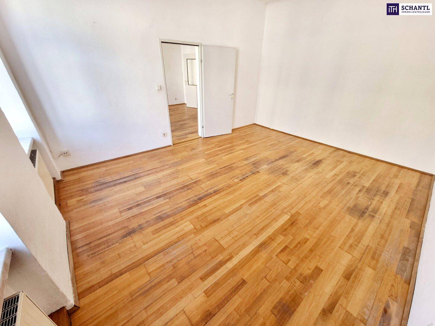 Geräumiger Raum mit Holzboden und weißen Wänden, der durch eine offene Tür verbunden ist.