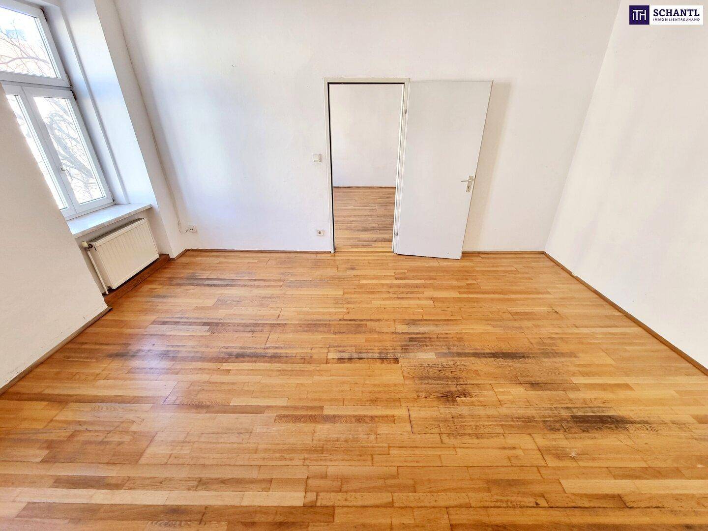 Leerer Raum mit Holzboden, weißen Wänden und einem Fenster, das Tageslicht hereinlässt.