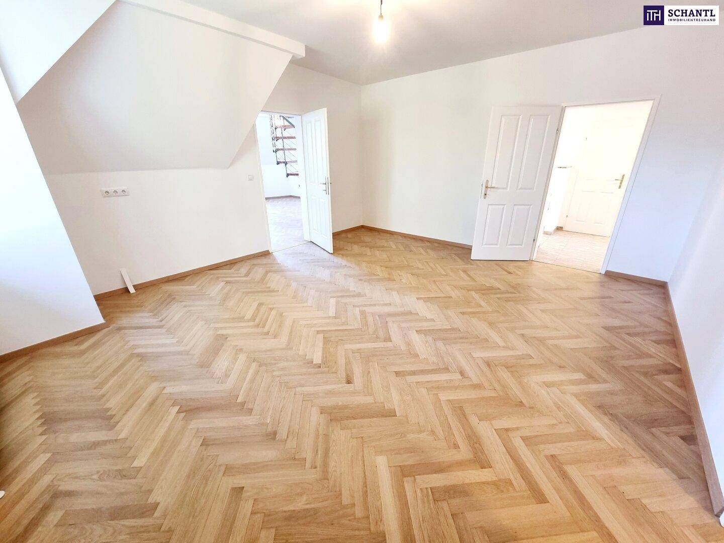 Geräumiger Dachgeschossraum mit Fischgrätparkett, Dachschrägen und weiß gestrichenen Wänden.