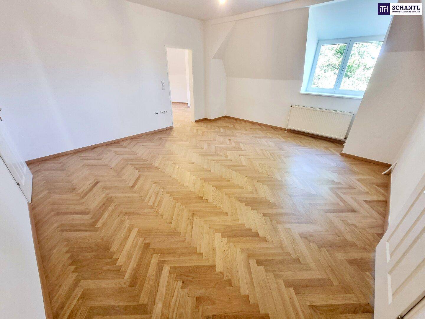 Lichtdurchflutetes Dachgeschosszimmer mit Fischgrätparkett, Dachschrägen und Fenster.