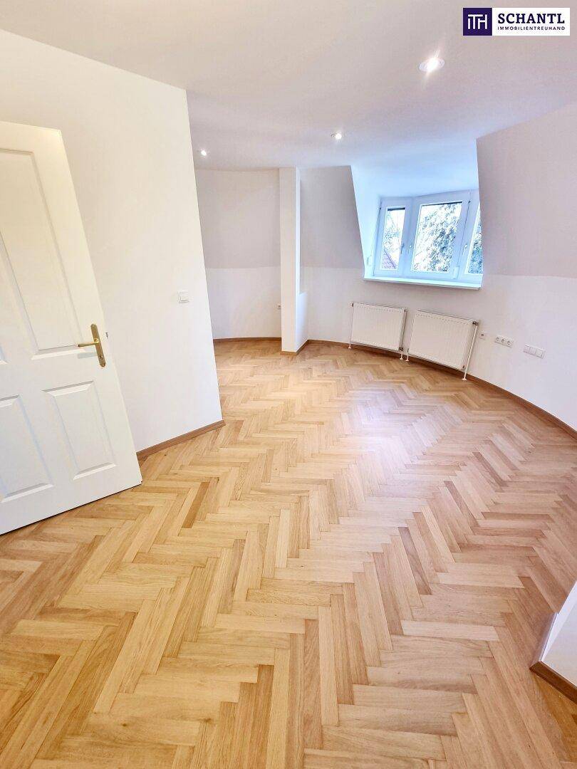 Dachgeschosszimmer mit hellem Fischgrätparkett und Fenstern für viel Tageslicht.