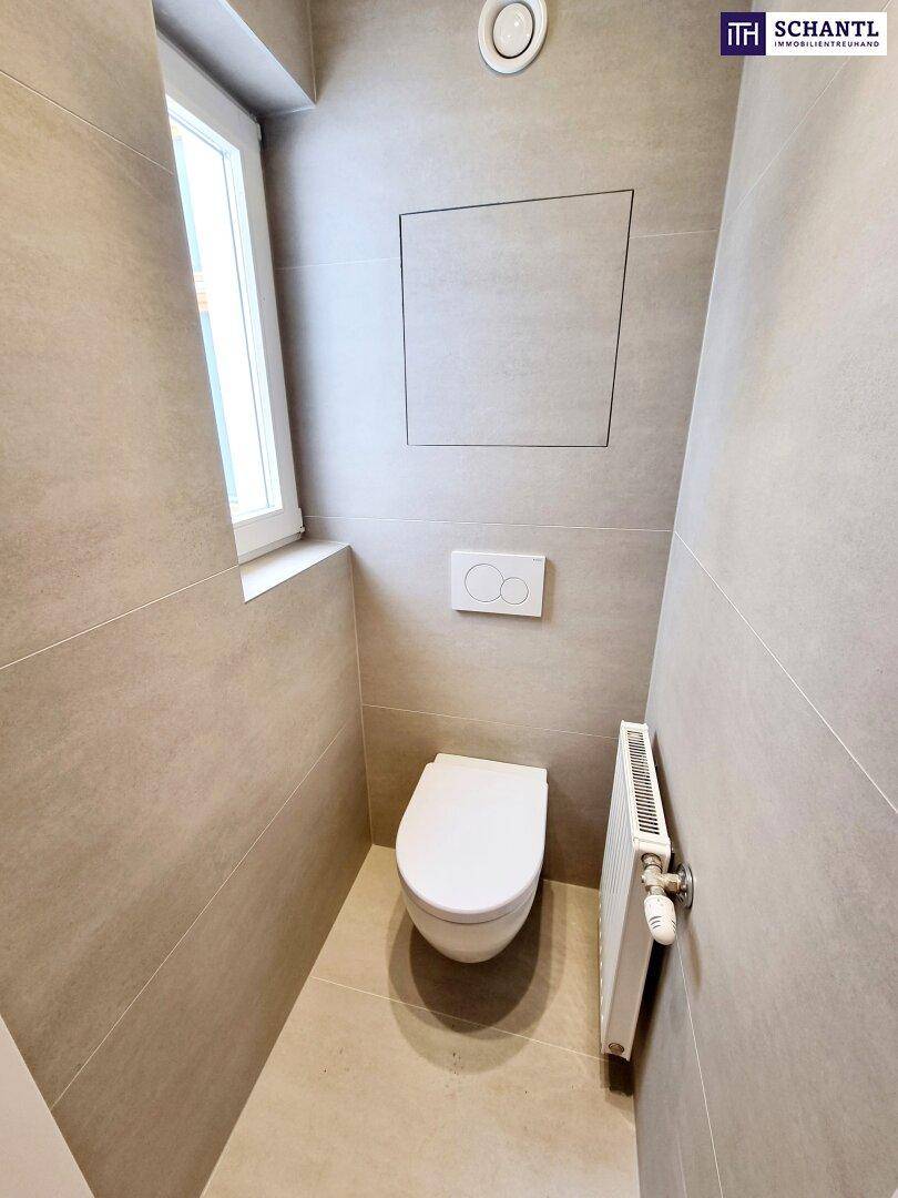 Modernes Gäste-WC mit wandhängender Toilette, Fenster und grauen Fliesen.