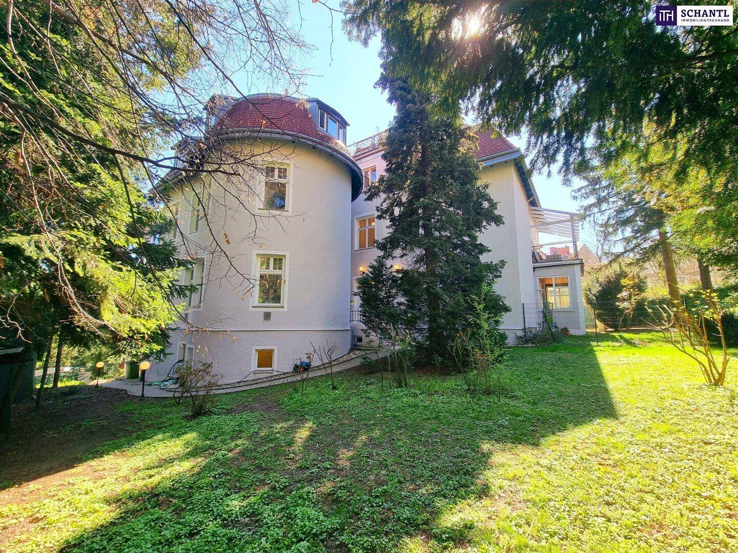 Historische Villa mit großem, gepflegtem Garten und altem Baumbestand an einem sonnigen Tag.