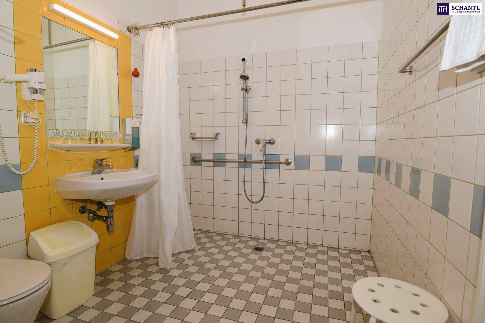 Barrierefreies Badezimmer mit ebenerdiger Dusche, Haltegriffen und gelben Akzentfliesen.