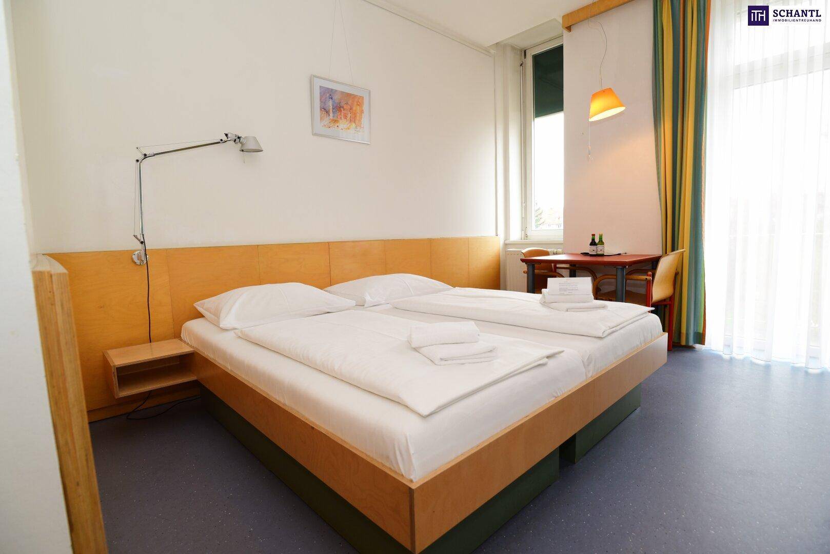 Helles Schlafzimmer mit zwei Einzelbetten, Holzmöbeln und einem großen Fenster.