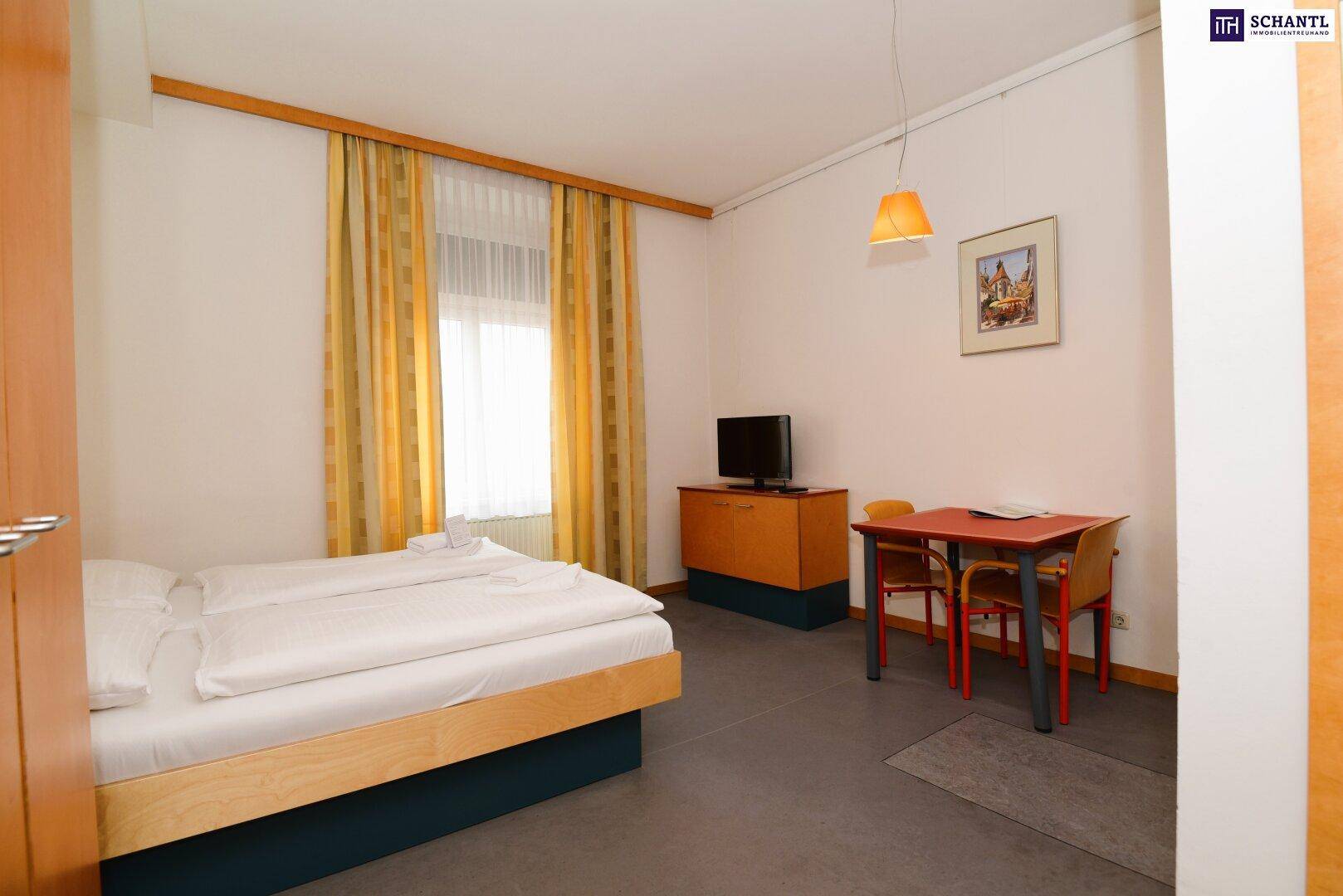 Schlichtes Schlafzimmer mit zwei Einzelbetten, kleinem Tisch und Fernseher.