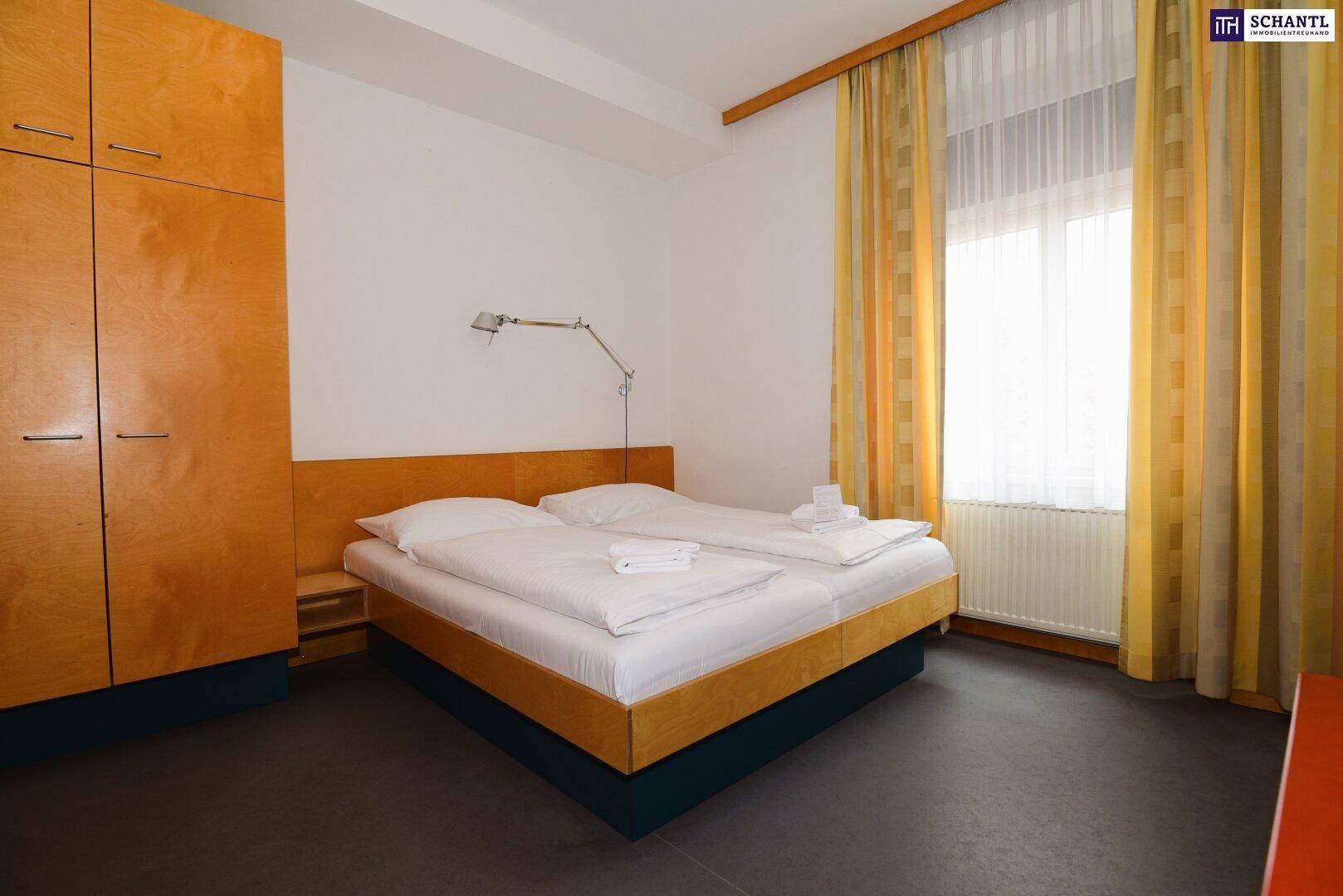 Schlafzimmer mit großem Fenster, Kleiderschrank und zwei Einzelbetten in einfacher Ausstattung.