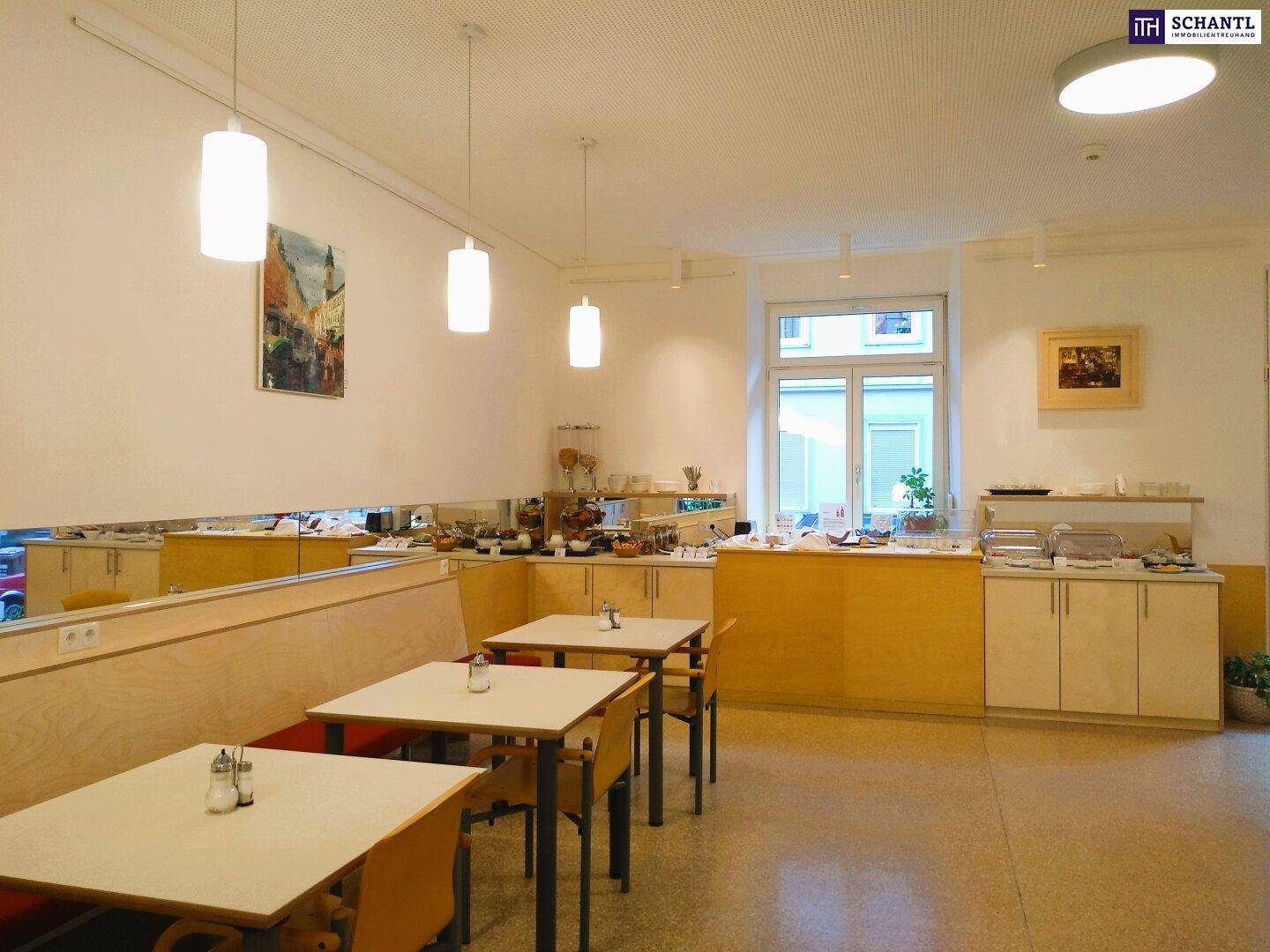 Großer Frühstücksraum mit Buffet, Tischen und Stühlen, gut beleuchtet durch Fenster.