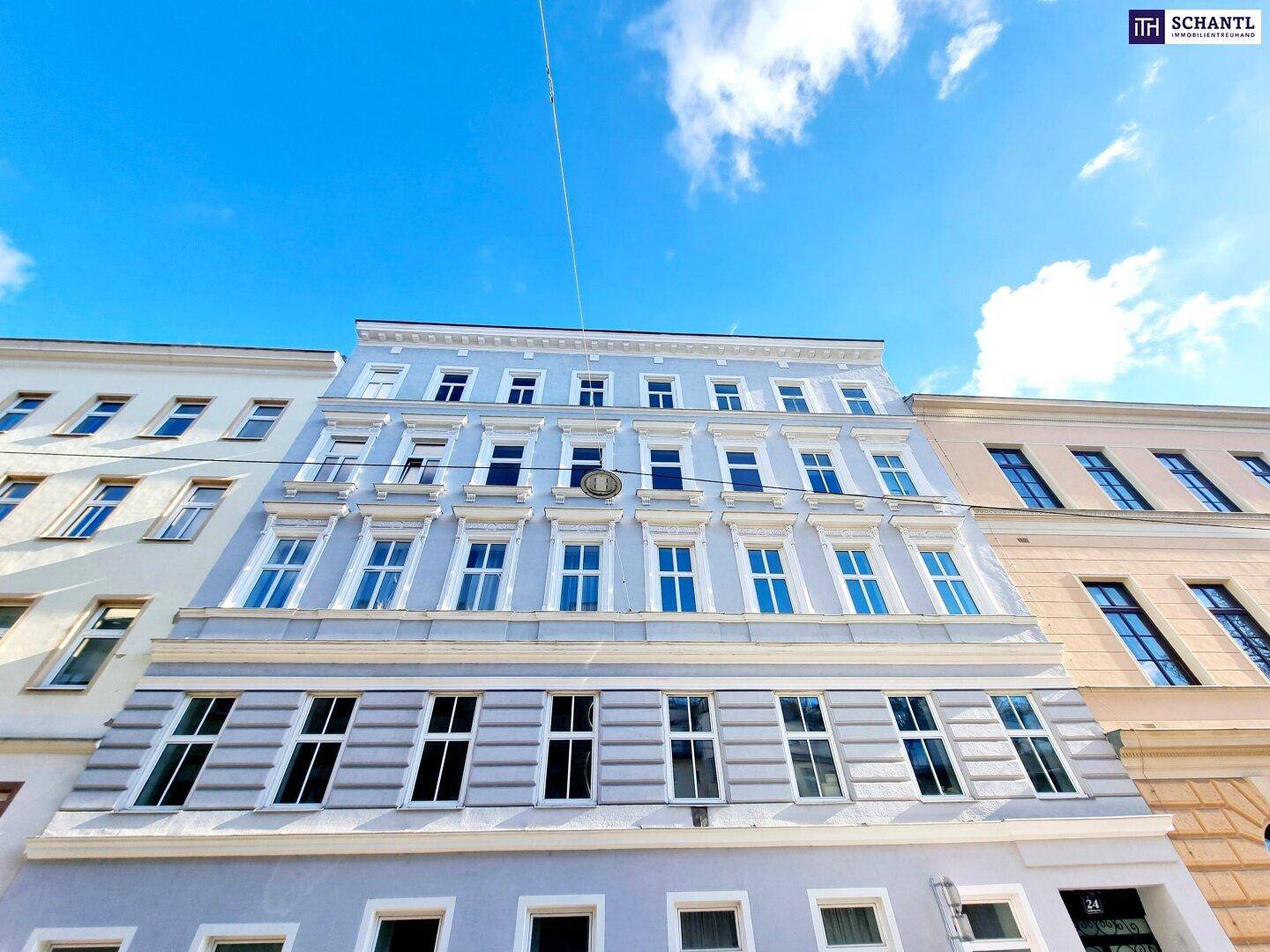 Historische Fassade eines Mehrfamilienhauses mit vielen Fenstern unter blauem Himmel.