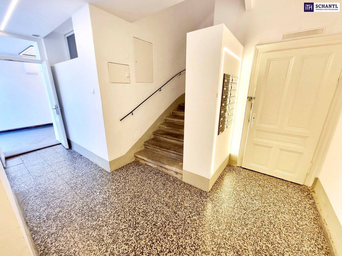 Heller Eingangsbereich mit Treppenaufgang, Terrazzoboden und Briefkästen.