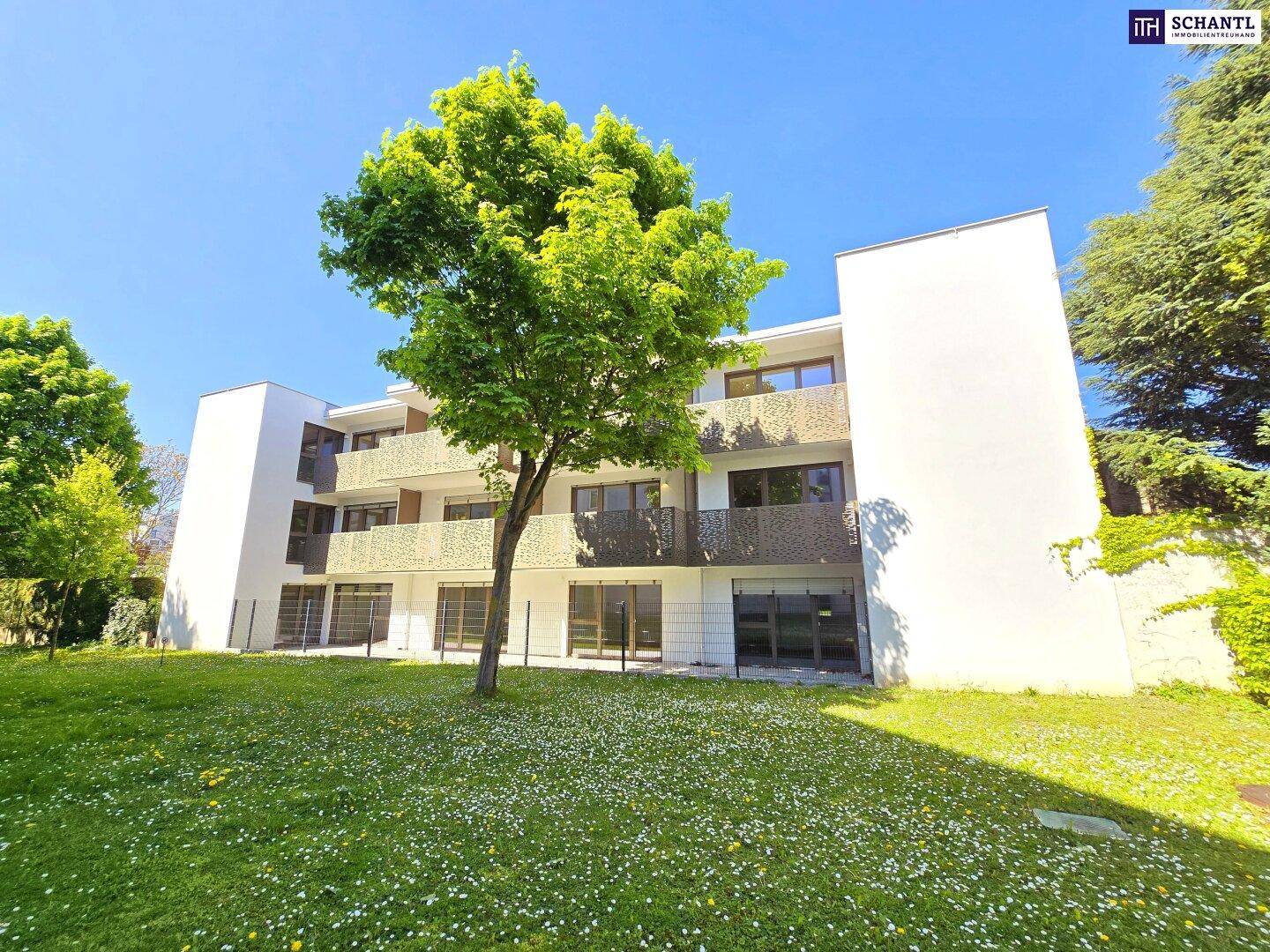 Weitläufiger grüner Gartenbereich vor einer modernen Wohnanlage mit Balkonen unter blauem Himmel.
