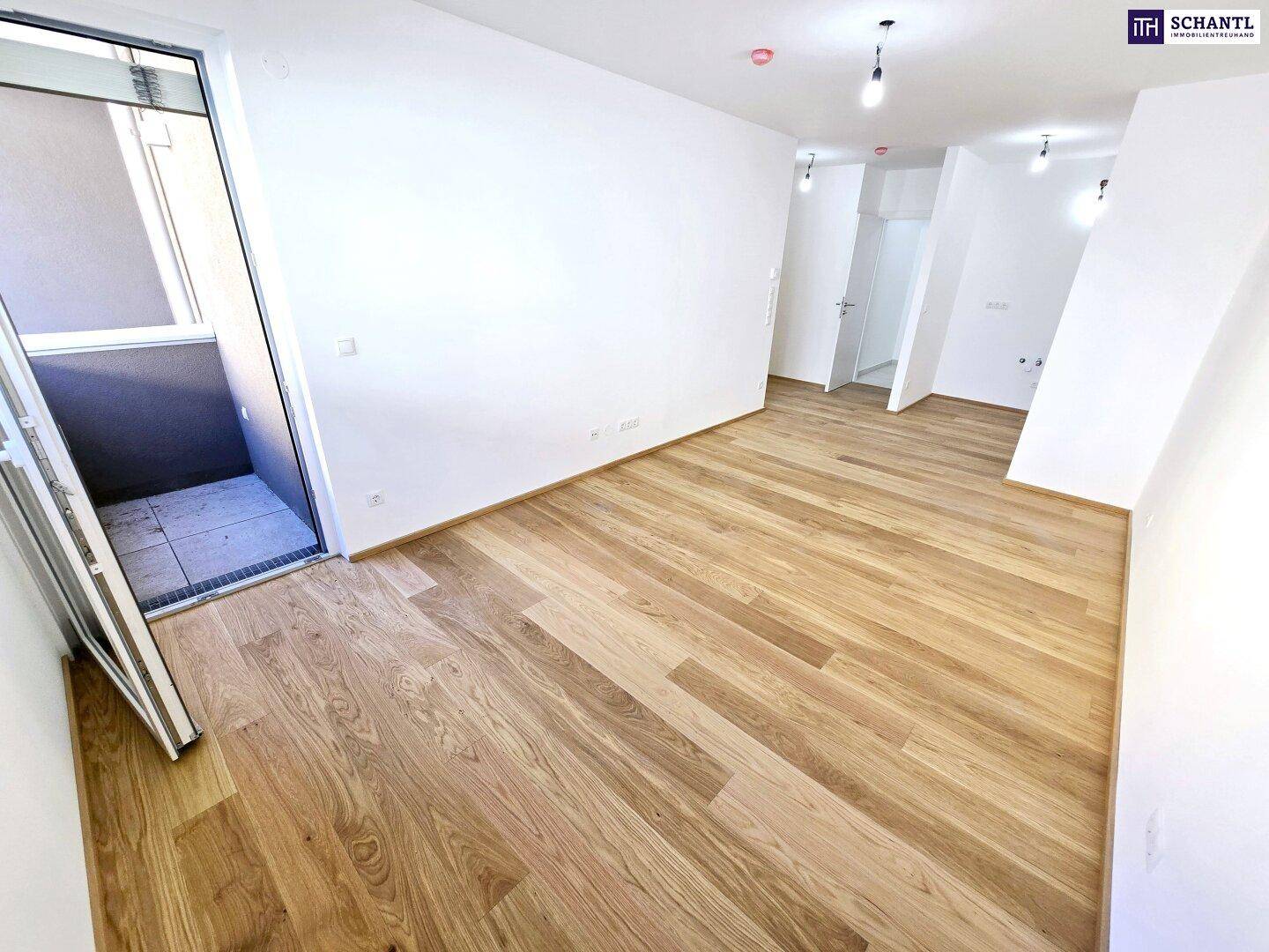 Heller, leerer Raum mit neuem Holzparkettboden und Zugang zu einem kleinen Balkon.