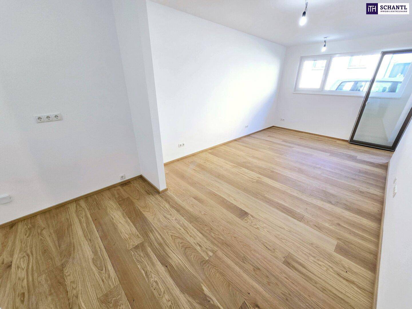 Heller Wohnraum mit Holzparkettboden und großem Fenster, das viel Tageslicht hereinlässt.