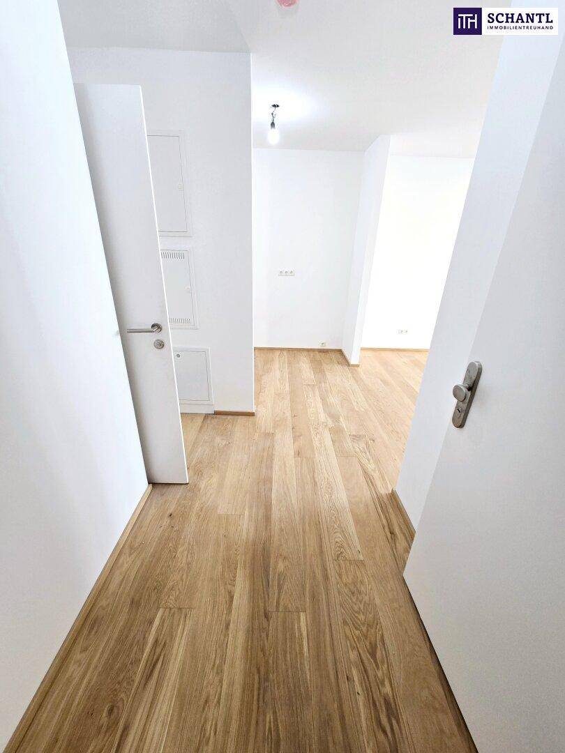 Heller Flur mit Holzparkettboden und weißen Wänden, der zu weiteren Räumen führt.