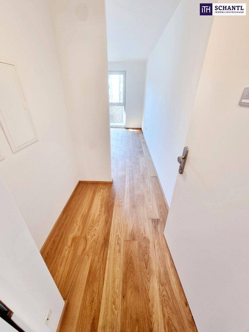 Schmaler Flur mit Holzparkettboden, der zu einem hellen Bereich mit Fenster führt.