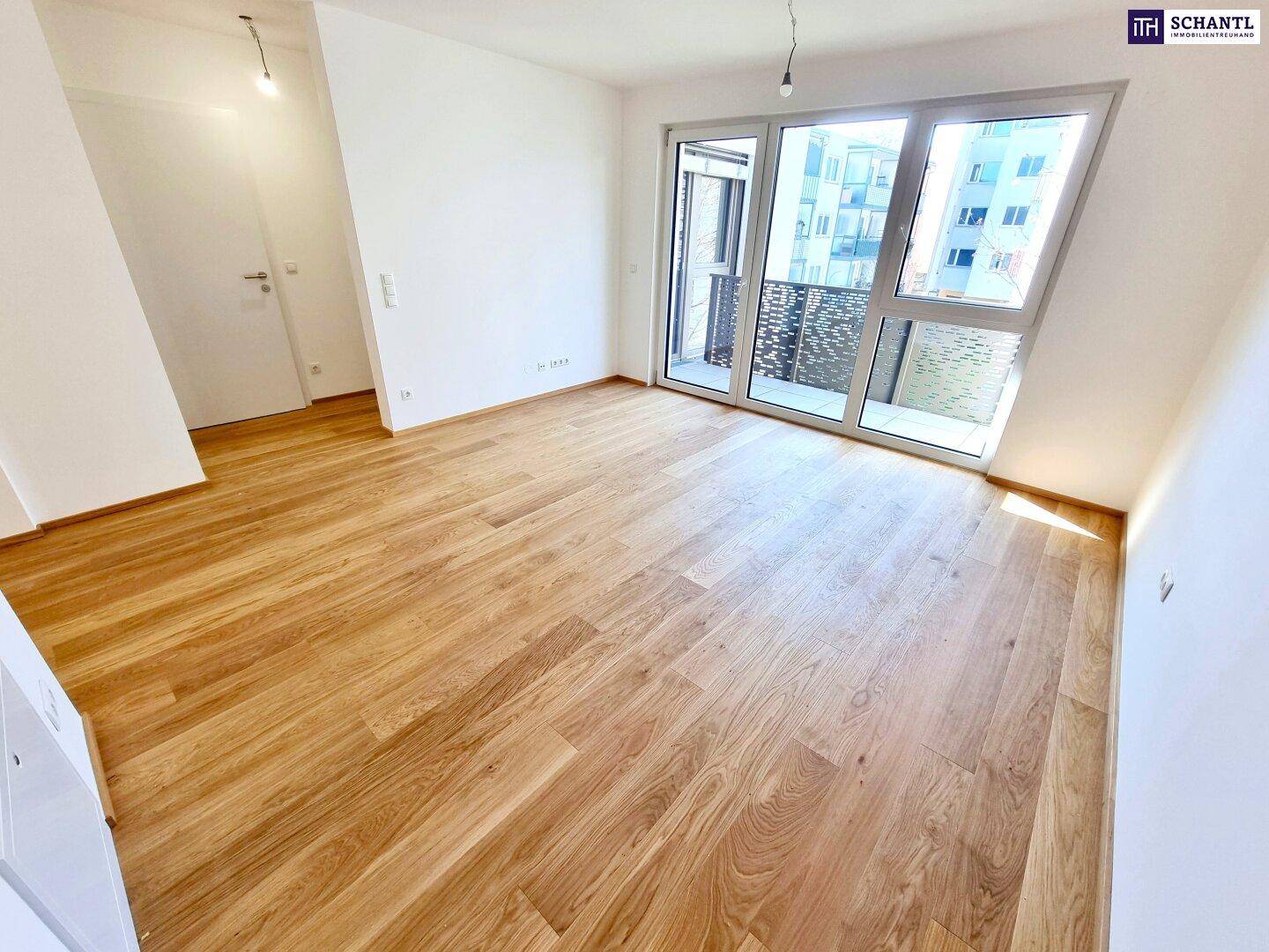 Helles, leeres Zimmer mit neuem Holzparkettboden und Zugang zu einem Balkon.
