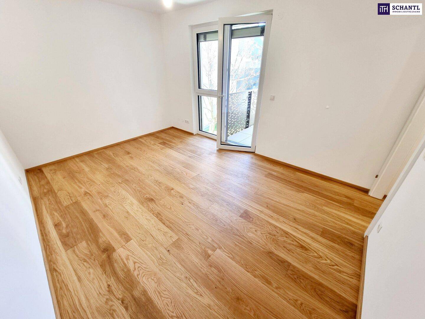 Leeres Zimmer mit Holzboden und großen Fenstern, die viel Tageslicht hereinlassen.