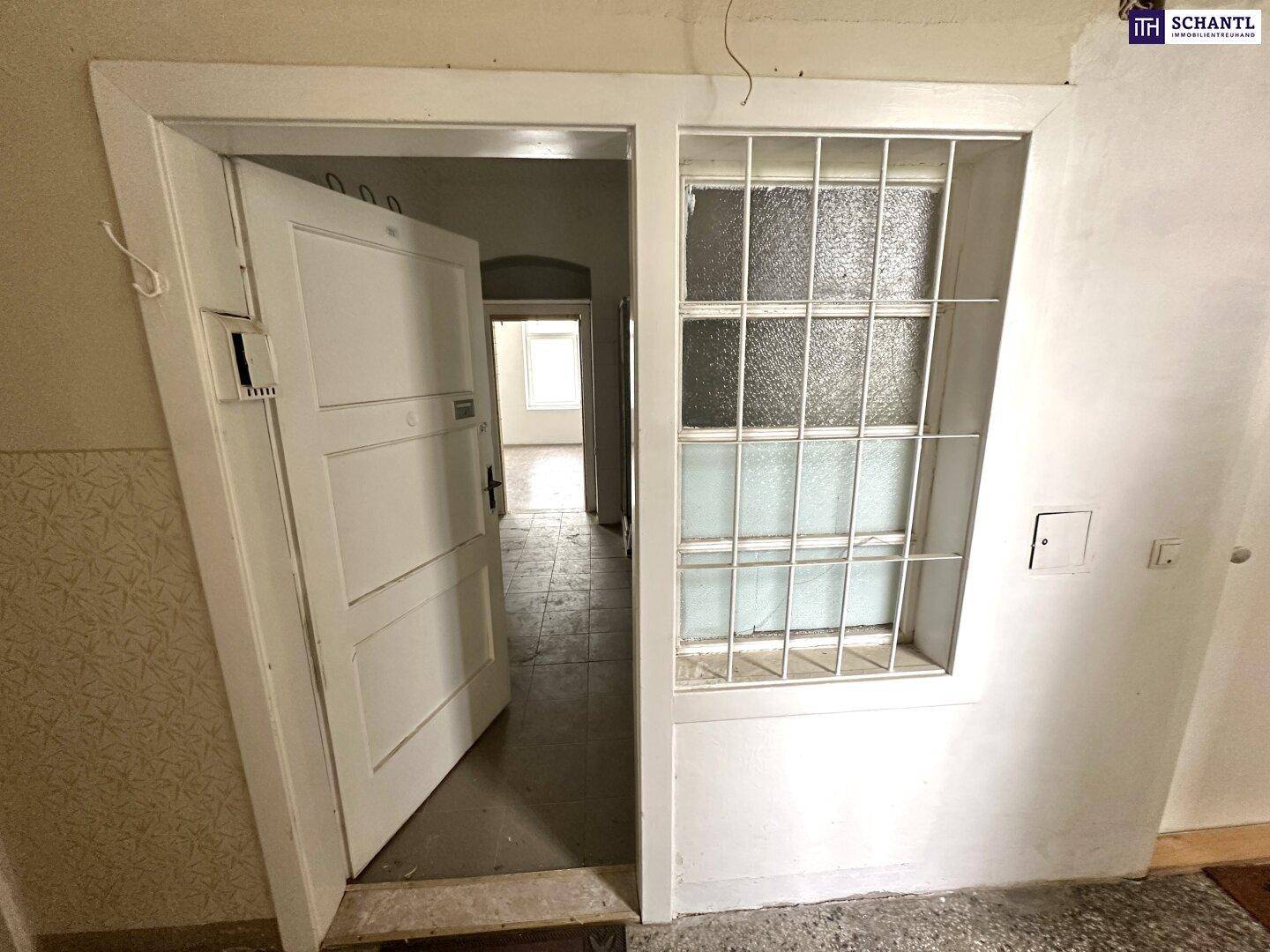 Eingangsbereich mit offener Tür zu einem weiteren Raum, Fenster mit Gitter und sichtbaren Gebrauchsspuren.