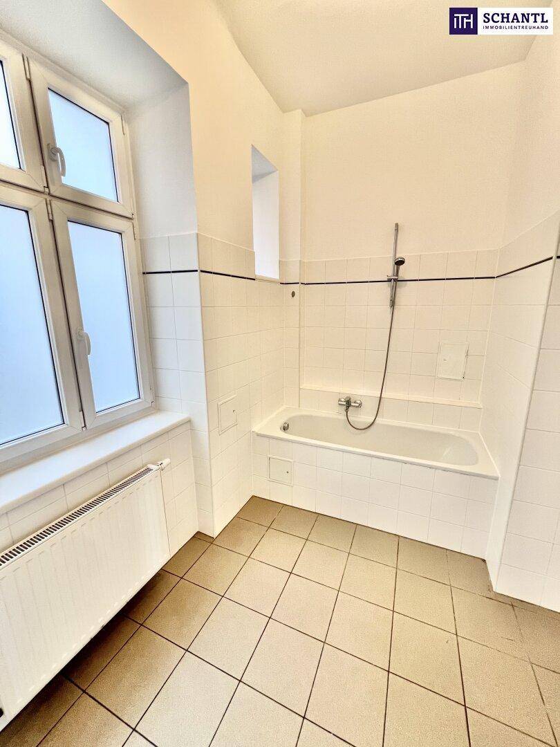 Helles Badezimmer mit Badewanne, weißen Fliesen und einem Fenster für natürliche Belüftung.