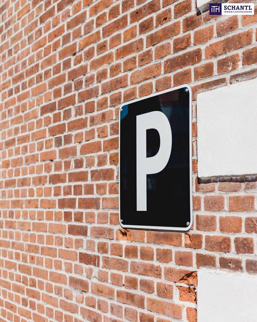 Ziegelwand mit einem schwarzen Parkplatzschild, das ein weißes 'P' zeigt, und einem angrenzenden weißen Wandbereich.