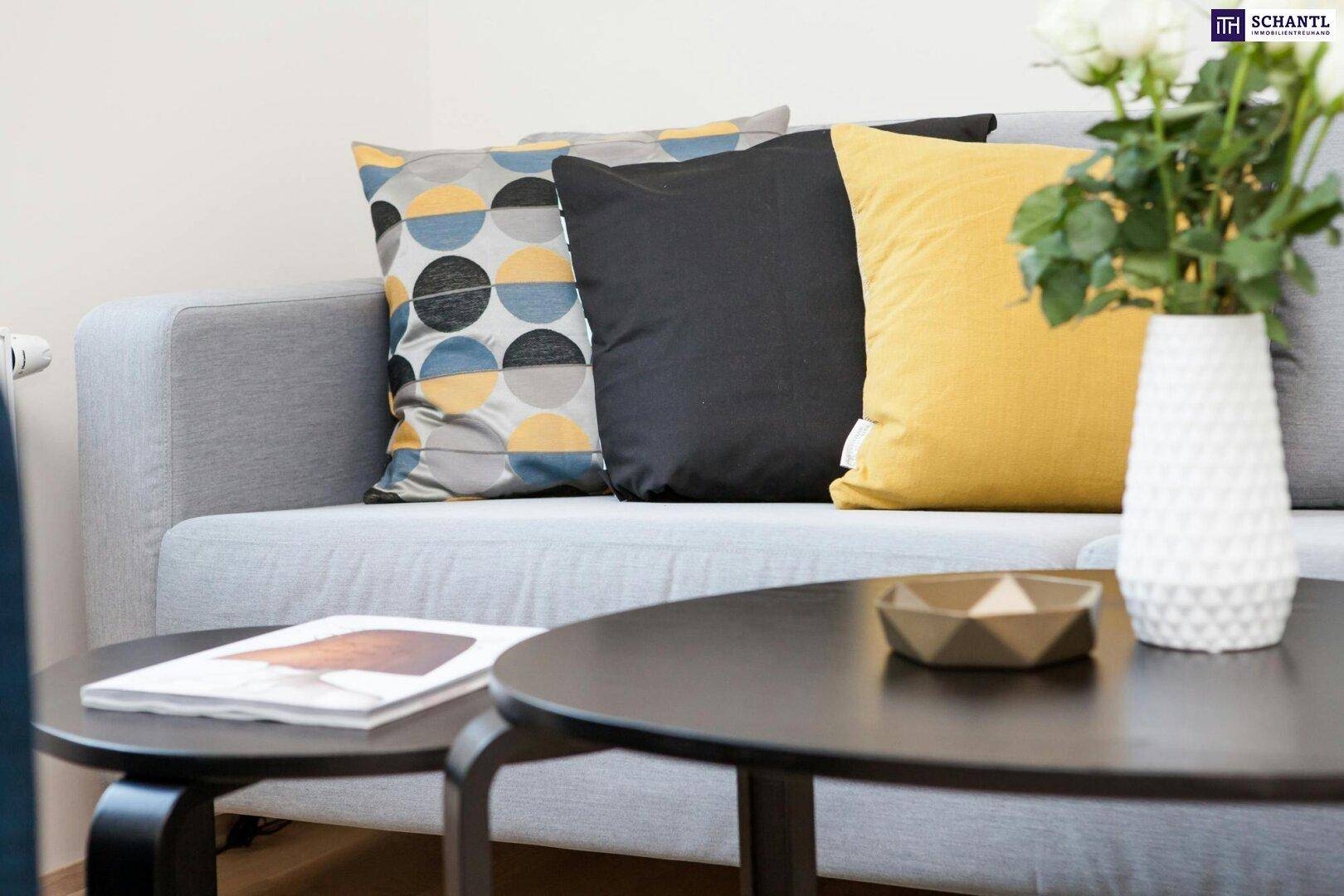 Gemütliches Sofa mit bunten Kissen und einem Couchtisch, dekoriert mit weißen Rosen.