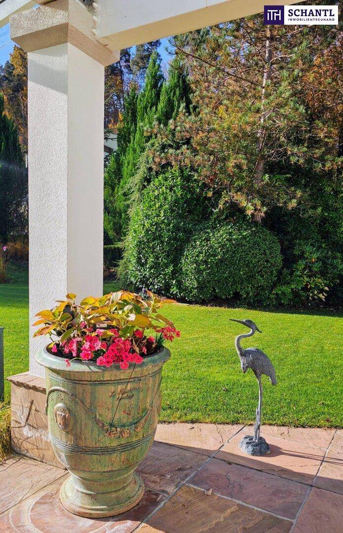 Dekorativer Blumentopf und Reiherstatue auf einer gepflasterten Fläche im sonnigen Gartenbereich.