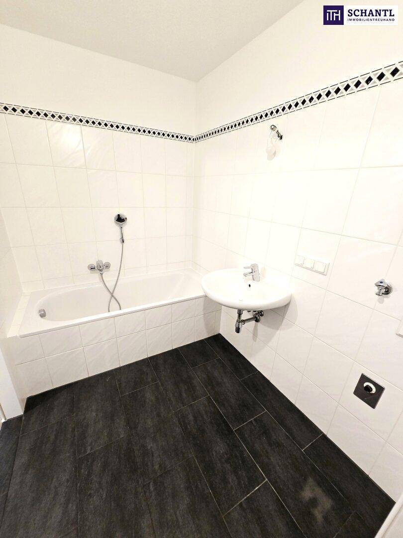Modernes Badezimmer mit Badewanne, Waschbecken und dunklen Bodenfliesen, akzentuiert durch eine Bordüre.