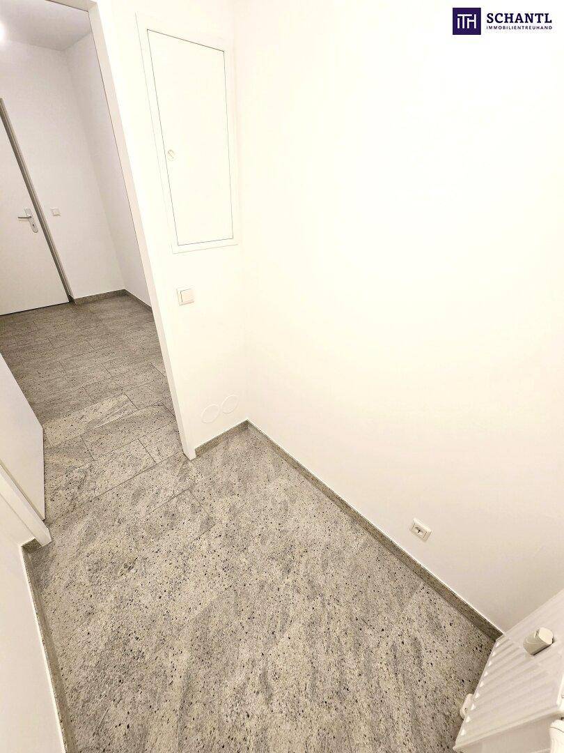 Heller Eingangsbereich mit robustem Fliesenboden und weiß gestrichenen Wänden, der zu den Zimmern führt.