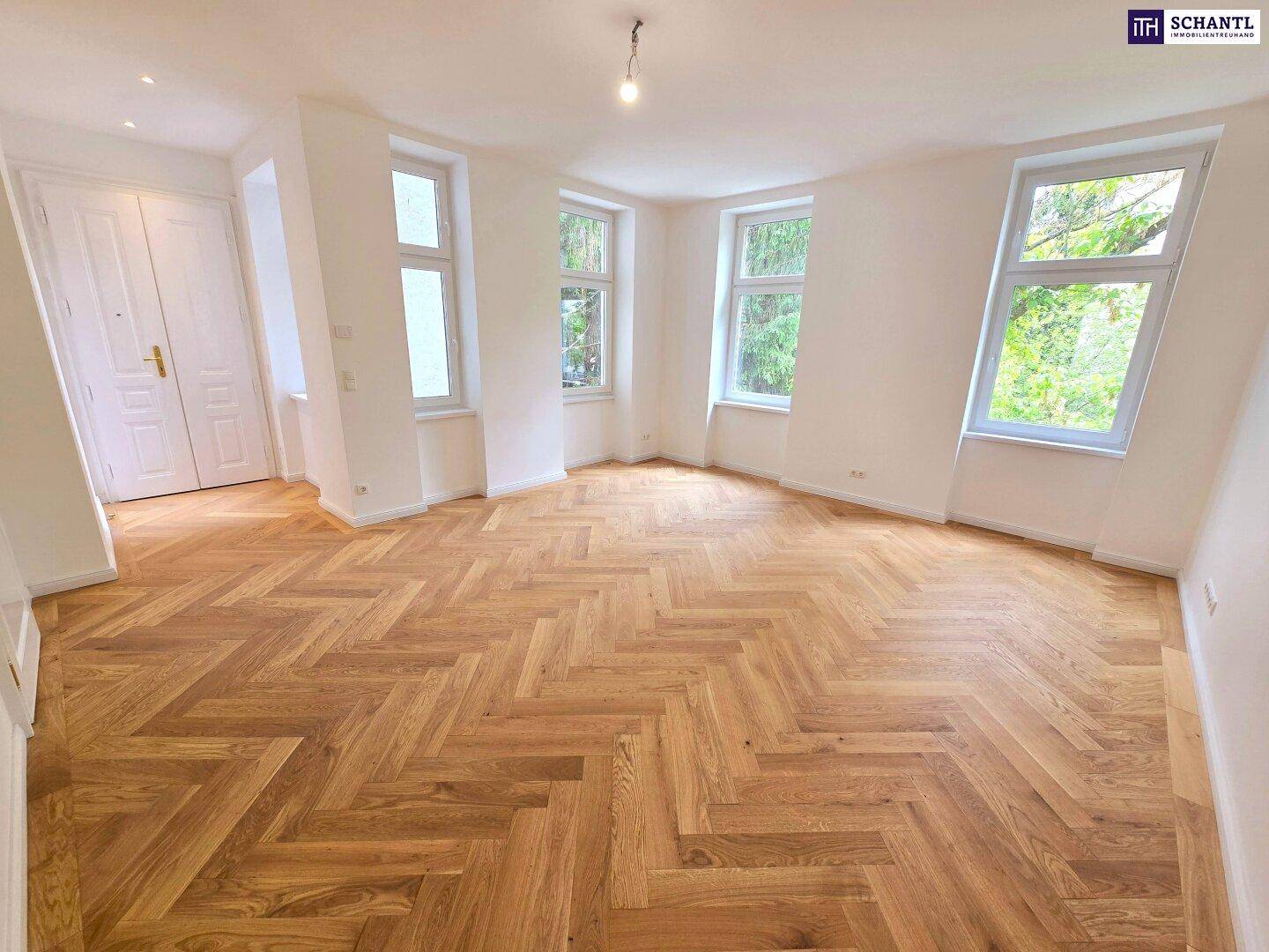 Großes, helles Zimmer mit Fischgrätparkett und vielen Fenstern, die viel Tageslicht hereinlassen.