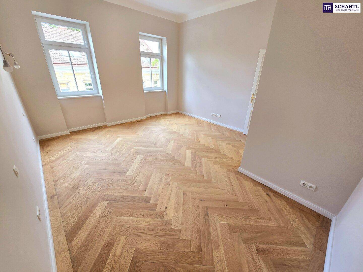 Helles Zimmer mit elegantem Fischgrätparkett und zwei Fenstern, bereit zur individuellen Gestaltung.