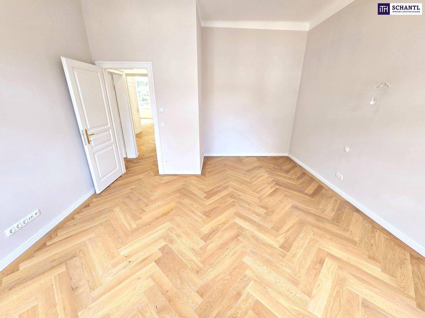 Geräumiges Zimmer mit klassischem Fischgrätparkett und offener Tür zu weiteren Bereichen.