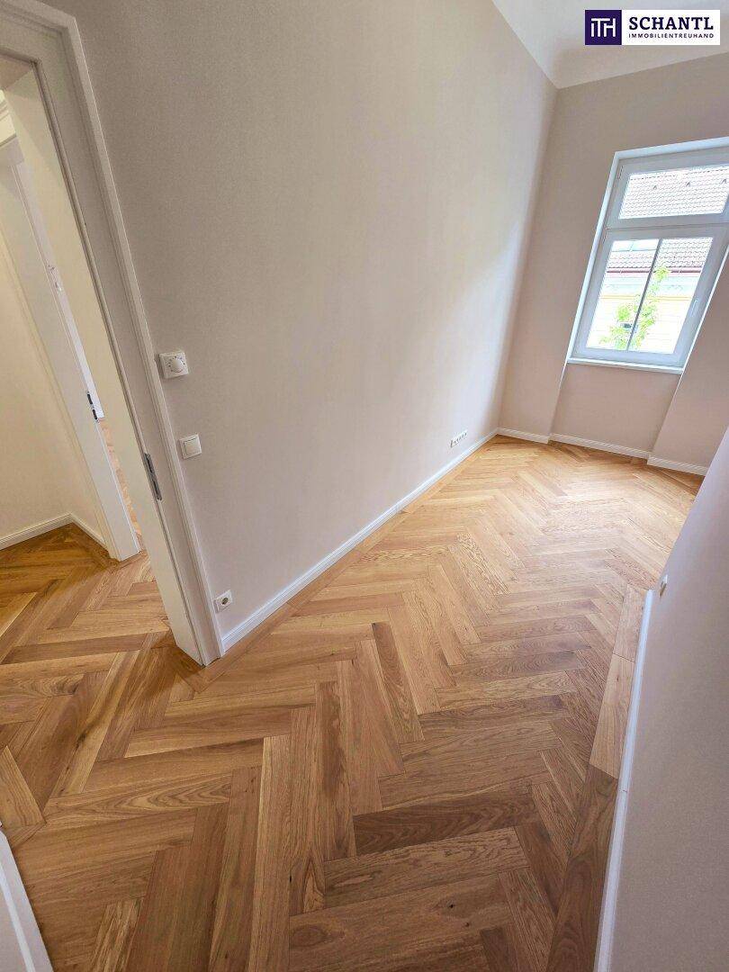 Helles Zimmer mit klassischem Fischgrätparkett und einem Fenster, das viel Tageslicht hereinlässt.