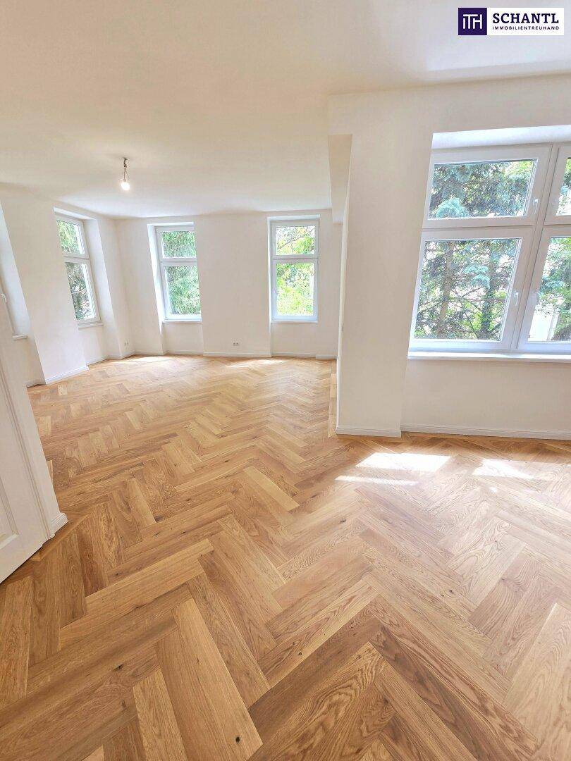 Geräumiger, heller Raum mit Fischgrätparkett und großen Fenstern mit Blick auf Bäume.